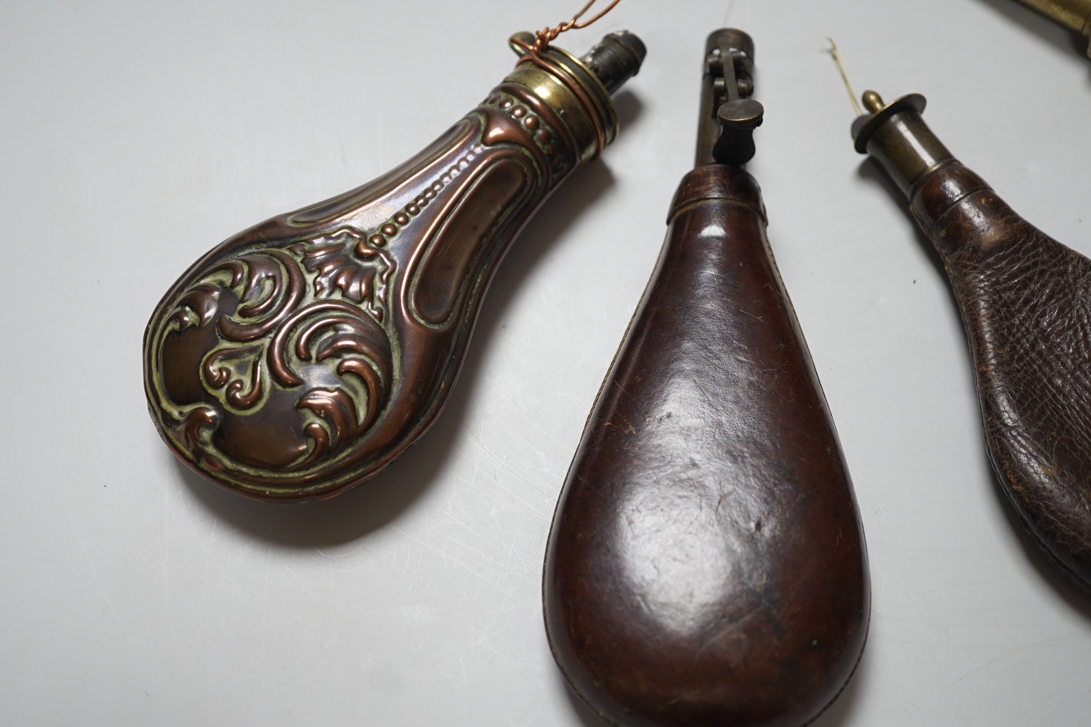 Four brass mounted powder flasks, to include three leather flasks, and one copper. Largest 24cm long